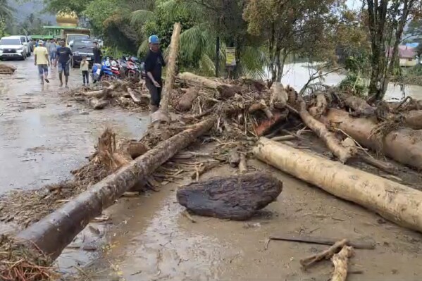 In this image made from video, a man attempts to remove logs that block a street following a flash flood in Langgai, West Sumatra, Indonesia, Sunday, March 10, 2024. Torrential rains have triggered flash floods and a landslide on Indonesia's Sumatra island leaving a number of people dead and missing, officials said Sunday. (AP Photo)