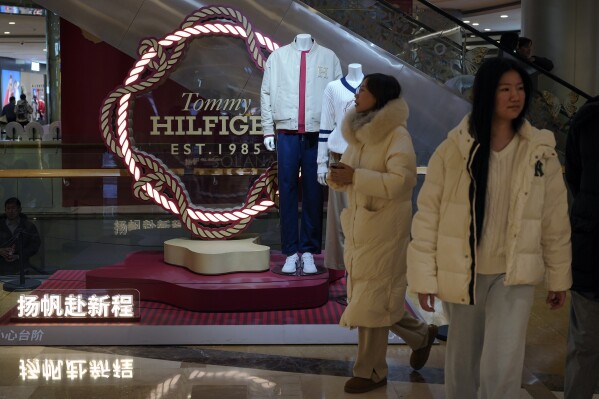 Women walk by a fashion display of Tommy Hilfiger, which is owned by PVH Group, at a shopping mall in Beijing, Tuesday, Feb. 4, 2025. (AP Photo/Andy Wong)