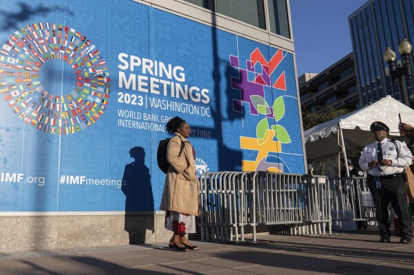 FILE - People pose for a photograph next to an International Monetary Fund banner, during the World Bank/IMF spring meetings at IMF headquarters in Washington, April 11, 2023. The International Monetary Fund has upgraded its outlook for the global economy in 2024, saying the world appears headed for a "soft landing" — reining in inflation without much economic pain and producing steady if modest growth. (AP Photo/Jose Luis Magana, File)