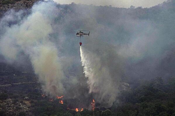 A helicopter drops water to put out flames are seen a wooded area in Cugliari, near Oristano, on the island of Sardinia, Italy, Monday, July 26, 2021. Fires raged Sunday on Italy's Mediterranean island of Sardinia, where nearly 400 people were evacuated overnight. No deaths or injuries have been reported. Firefighters said several homes were damaged in the island's western interior region. (Alessandro Tocco/LaPresse via AP)