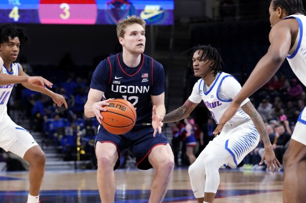 UConn guard Cam Spencer (12) drives as DePaul guard Keyondre Young, left, guard Jalen Terry and center Churchill Abass, right, guard during the first half of an NCAA college basketball game in Chicago, Wednesday, Feb. 14, 2024. (AP Photo/Nam Y. Huh)