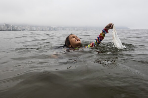 FILE - Nina Gomes recovers a discarded plastic bag from ocean waters, near Copacabana beach in Rio de Janeiro, Brazil, March 19, 2024. (AP Photo/Bruna Prado, File)