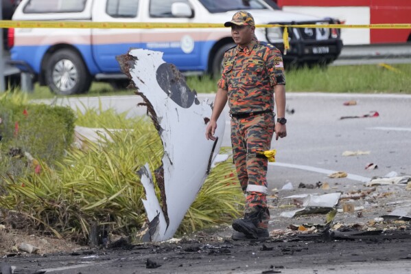 A member of the fire and rescue department inspect the crash site of a small plane in Shah Alam district, Malaysia, Thursday, Aug. 17, 2023. Police say a small aircraft has crashed in the suburb of Malaysia's central Selangor state, with multiple bodies recovered. (AP Photo/Vincent Thian)