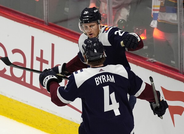 Colorado Avalanche defenseman Bo Byram (4) congratulates center Nathan MacKinnon, top, after MacKinnon scored in the second period of an NHL hockey game against the Arizona Coyotes, Sunday, Feb. 18, 2024, in Denver. (AP Photo/David Zalubowski)