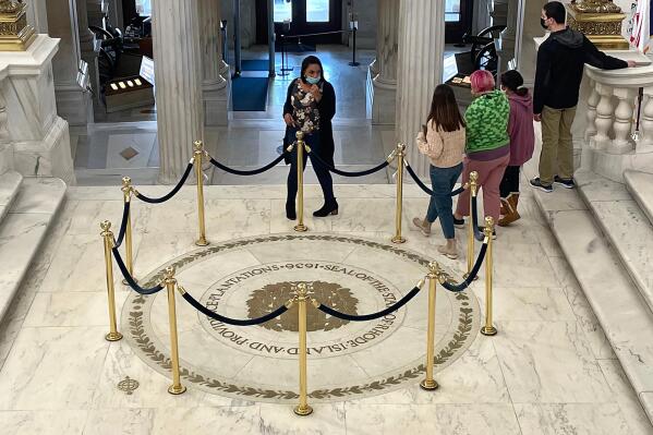 Visitors to the Rhode Island State House, in Providence, R.I., pass by the state seal on the rotunda floor that displays Rhode Island's full former name, Thursday, Nov. 4, 2021. Voters chose to strip the words "and Providence Plantations" from Rhode Island's formal name a year ago by approving a statewide referendum that was revived amid the nation's reckoning with racial injustice following the murder of George Floyd. The phrase remains on walls, doors, floors and rugs. (AP Photo/Jennifer McDermott)