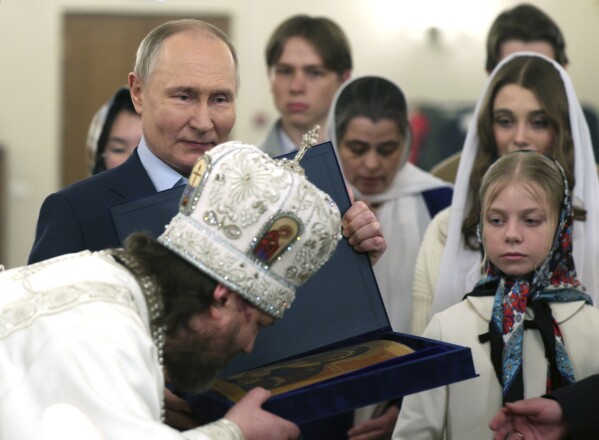 Russian Orthodox Archbishop of Odintsovo and Krasnogorsk Foma (Nikolay Mosolov), foreground, kisses an icon as Russian President Vladimir Putin, left, stands near after attending an Orthodox Christmas service with the families of military personnel who died during the special military operation in Ukraine in the Church of Our Savior Not Made by Hands at the Novo-Ogaryovo state residence outside Moscow, Russia, on Sunday, Jan. 7, 2024. (Gavriil Grigorov, Sputnik, Kremlin Pool Photo via AP)