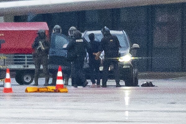 A man is led away by the police at the airport in Hamburg, Germany, Sunday, Nov. 5, 2023. The hostage situation at Hamburg Airport has ended around 18 hours after a man drove his vehicle through the gates of the airport with his 4-year-old daughter inside. Police said Sunday that the man was arrested and the girl appears to be unharmed. (Jonas Walzberg/dpa via AP)