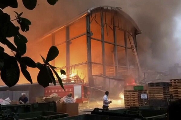 In this image made from video footage run by FTV, people watch a fire from a factory of golf ball manufacturer Launch Technologies Co. in the southern county of Pingtung in Taiwan on Friday, Sept. 22, 2023. Search teams found more bodies on Sunday at the site of a golf ball factory fire in southern Taiwan, according to Taiwanese media reports. (FTV via AP)