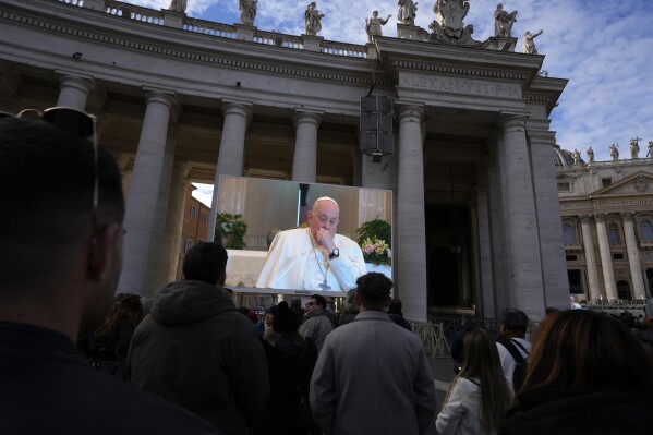 A giant screen broadcasts Pope Francis coughing during the Angelus noon prayer, from the chapel of the hotel at the Vatican grounds where he lives, Sunday, Nov. 26, 2023. Pope Francis says he has a lung inflammation but will go later this week to Dubai for the climate change conference. Francis skipped his weekly Sunday appearance at a window overlooking St. Peter's Square, a day after the Vatican said he was suffering from a mild flu. (AP Photo/Alessandra Tarantino)