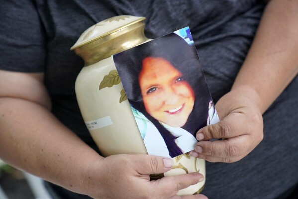 FILE- Kelly Titchenell sits on her porch in Mather, Pa., holding a photo of her mother Diania Kronk, and an urn containing her mother's ashes, July 7, 2022. Prosecutors this week dropped an involuntary manslaughter case against a 911 dispatcher in Pennsylvania who had been accused of failing to send an ambulance to the rural home of the woman who was found dead a day later of internal bleeding. (AP Photo/Gene J. Puskar, File)