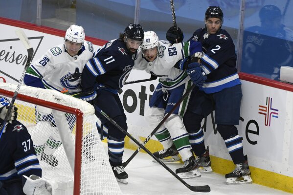 Winnipeg Jets' Nate Thompson (11) and Dylan DeMelo (2) and Vancouver Canucks' Antoine Roussel (26) and Jay Beagle (83) battle for the puck behind the Jets net during first period NHL hockey action in Winnipeg, Manitoba on Tuesday March 1, 2021. (Fred Greenslade/The Canadian Press via AP)