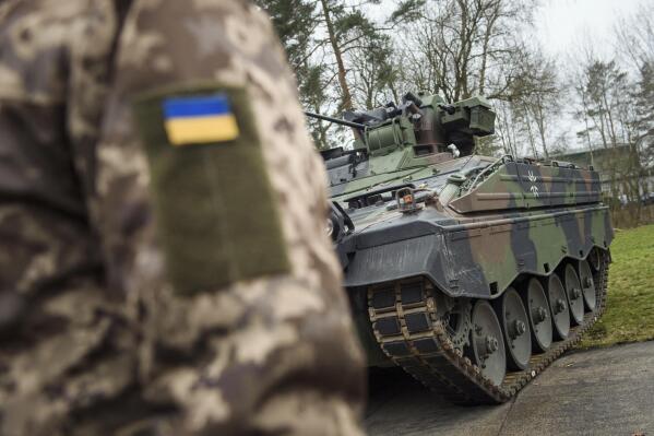 FILE - A Ukrainian soldier is standing in front of a Marder infantry fighting vehicle at the German forces Bundeswehr training area in Munster, Germany, Monday, Feb. 20, 2023. Germany said Saturday, May 13, 2023 it is providing Ukraine with additional military aid worth more than 2.7 billion euros ($3 billion), including tanks, anti-aircraft systems and ammunition. The announcement Saturday came as preparations were underway in Berlin for a possible first visit to Germany by Ukrainian President Volodymyr Zelenskyy since Russia invaded his country last year. (AP Photo/Gregor Fischer, File)