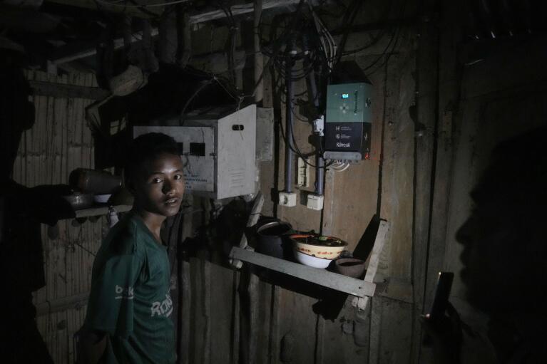 Antonius Pekambani stands near the control console for the solar panel unit installed at his house in Ndapayami village on Sumba Island, Indonesia, Monday, March 20, 2023. "I couldn't really study at night before," said Pekambani, a student in Ndapaymi village, east Sumba. "But now I can." (AP Photo/Dita Alangkara)