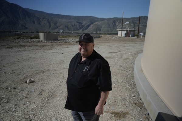 Mark Whaling, a retired firefighter, stands in front of a Heli-Hydrant, a small, open tank that helicopters can rely on to get water faster for urban fires, Friday, April 11, 2025, in Cabazon, Calif. (AP Photo/Brittany Peterson)