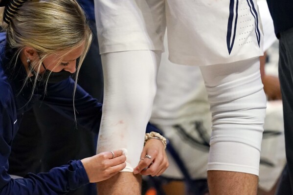 FILE - A trainer cleans blood off of the uniform of Xavier forward Jack Nunge (24) during the second half of an NCAA college basketball game against Butler, Wednesday, Feb. 2, 2022, in Cincinnati. Colleges and universities are having a difficult time hiring, recruiting and retaining members of their athletic training staffs because of a number of below-market conditions, a survey shows. (AP Photo/Jeff Dean, File)