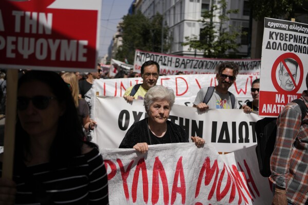 Protesters hold banners during a rally in Athens, Greece, Wednesday, April 17, 2024. A 24-hour strike called by Greece's largest labor union have halted ferries and public transport services in the Greek capital and other cities, to press for a return of collective bargaining rights axed more than a decade ago during a severe financial crisis. Writing on banner with red line across the face of Greece’s Prime Minister, Kyriakos Mitsotakis, reads in Greek; “Killer Government / We Will Overturn It”. (AP Photo/Thanassis Stavrakis)