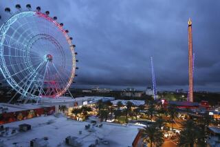 ICON Park attractions, The Wheel, left, Orlando SlingShot, middle, and Orlando FreeFall, right, are shown in Orlando, Fla., on March 24, 2022. The amusement park where a teenager fell from a ride and died earlier this year has paused a new sniper-like laser shooting game amid criticism in light of recent mass shootings. In a statement issued Saturday, July 16, 2022 park officials said some had questioned whether it was appropriate following mass shootings at a July 4 parade in a Chicago suburb, an elementary school in Ulvade, Texas and a grocery store in Buffalo, New York. (Stephen M. Dowell/Orlando Sentinel via AP, file)