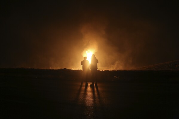 Two men look at flames after a natural gas pipeline explodes outside the city of Boroujen in the western Chaharmahal and Bakhtiari province, Iran, in early Wednesday, Feb. 14, 2024. Explosions struck a natural gas pipeline in Iran early Wednesday, with an official blaming the blasts on a 