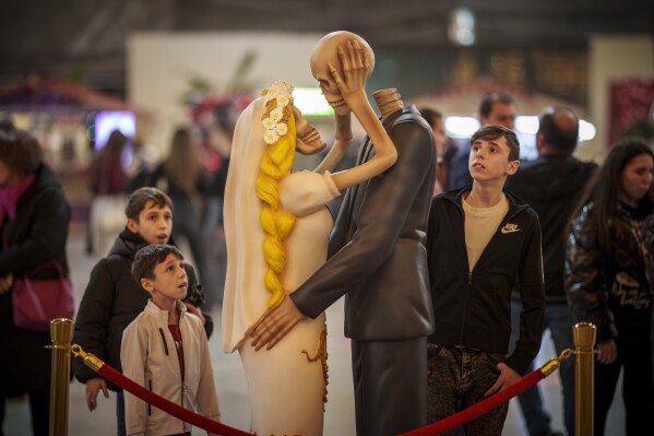 People look at a skeleton couple kissing installation dubbed " 'Till Death Do Us Part" during a Valentine's Day event in Bucharest, Romania, Tuesday, Feb. 13, 2024. (AP Photo/Vadim Ghirda)