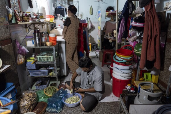 Pham Van Sang, a street food vendor and migrant from the Mekong Delta, prepares vegetables for the next day's business as his wife, Luong Thi Ut, chats via video with their daughter in their apartment in Ho Chi Minh City, Vietnam, Monday, Jan. 22, 2024. The couple works in the city's industrial zone, a common destination for many migrants from the Mekong Delta in search of a better life. (AP Photo/Jae C. Hong)