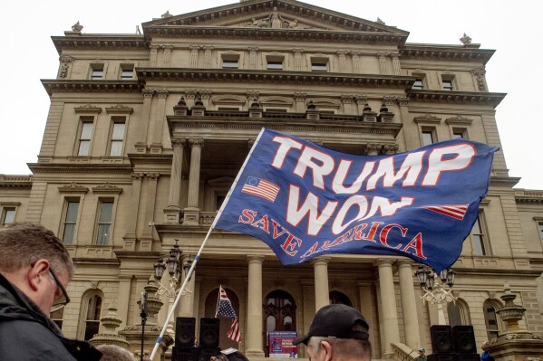 FILE - A protester waves a Trump flag during rally organized by a group called Election Integrity Fund and Force at the Michigan State Capitol, Tuesday, Oct. 12, 2021, in Lansing, Mich. Michigan Attorney General Dana Nessel has charged 16 Republicans Tuesday, July 18, 2023, with multiple felonies after they are alleged to have submitted false certificates stating they were the state’s presidential electors despite Joe Biden’s 154,000-vote victory in 2020. The group includes Republican National Committeewoman Kathy Berden and Meshawn Maddock, former co-chair of the Michigan Republican Party. (Jake May/The Flint Journal via AP, File)
