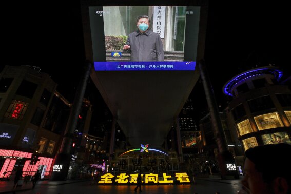 FILE - In this Tuesday, March 10, 2020 file photo, people walk by a giant TV screen at a quiet shopping mall in Beijing broadcasting news of Chinese President Xi Jinping talking to medical workers at the Huoshenshan Hospital in Wuhan in central China's Hubei Province, as he visited the center of the global virus outbreak. The government is handing out hundreds of thousands of dollars in grants to scientists researching the virus’ origins in southern China and with the military, The Associated Press has found. But it is monitoring their findings and mandating that the publication of any data or research must be approved by a new task force managed by China’s cabinet, under direct orders from President Xi Jinping, according to internal documents obtained by the AP. (AP Photo/Andy Wong)