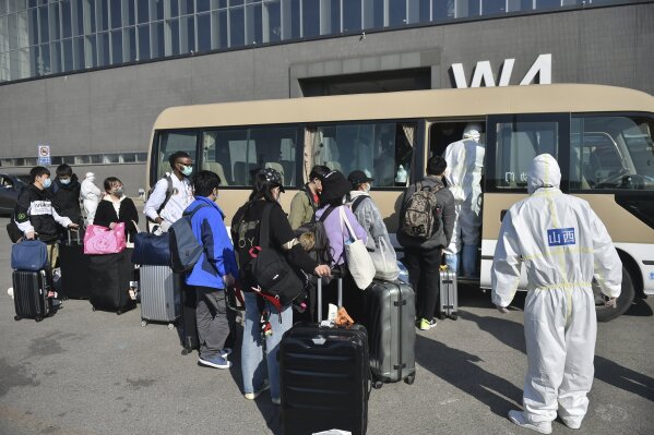 In this March 17, 2020, photo released by China's Xinhua News Agency, workers in protective suits watch as travelers board a shuttle bus at the New China International Exhibition Center, which has been converted into a facility to screen international flight passengers arriving in Beijing. As the pandemic expanded its reach, China and South Korea were trying to hold their hard-fought gains. China is quarantining new arrivals, who in recent days have accounted for an increasing number of cases, and South Korea starting Thursday will increase screenings of all overseas arrivals. The virus causes only mild or moderate symptoms, such as fever and cough, for most people, but severe illness is more likely in the elderly and people with existing health problems. (Peng Ziyang/Xinhua via AP)