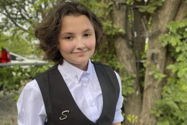 In this image provided Malia Pila, Nex Benedict poses outside the family's home in Owasso, Okla., in December 2023. A recently released police search warrant reveals more details in the case of Nex Benedict, a nonbinary Oklahoma student who died a day after a high school bathroom fight that may have been prompted by bullying over gender identity. (Sue Benedict via AP)