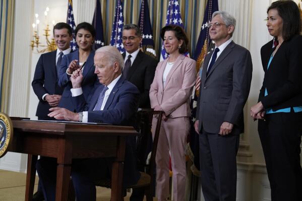 President Joe Biden hands out a pen after signing an executive order aimed at promoting competition in the economy, in the State Dining Room of the White House, Friday, July 9, 2021, in Washington. Standing from left, Transportation Secretary Pete Buttigieg, Lina Khan, Chair of the Federal Trade Commission, Health and Human Services Secretary Xavier Becerra, Commerce Secretary Gina Raimondo, Attorney General Merrick Garland, National Economic Council director Brian Deese, obscured, and Jessica Rosenworcel, Acting Chairwoman of the Federal Communications Commission. (AP Photo/Evan Vucci)