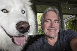 In this April 5, 2020, photo, Michael Liedtke poses with Wookiee, his newly adopted dog, while sheltering in place in Berkeley, Calif. While millions of people are stuck in their homes, there are abandoned dogs and cats still looking for one. (AP Photo/Michael Liedtke)