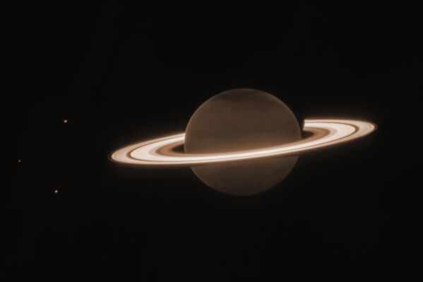 This June 2023 image provided by the Space Telescope Science Institute shows the planet Saturn and three of its moons, from left, Enceladus, Tethys and Dione, captured by the James Webb Space Telescope. In infrared, the planet appears dark because sunlight is absorbed by methane in the atmosphere. (NASA, ESA, CSA, JWST Saturn Team via AP)