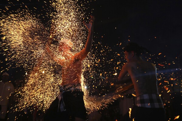 A Hindu devout hits another with burning coconut leaves, sending sparks and embers flying in all directions, in a ritual known as Lukat Gni, as part of Balinese Hindu New Year celebrations, in Bali, Indonesia on Sunday, March 10, 2024. (AP Photo/Firdia Lisnawati)