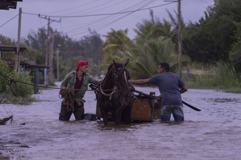 People traverse a flooded street with a horse-drawn carriage after the passage of Hurricane Helene in Guanimar, Artemisa province, Cuba, Wednesday, Sept. 25, 2024. (AP Photo/Ramon Espinosa)