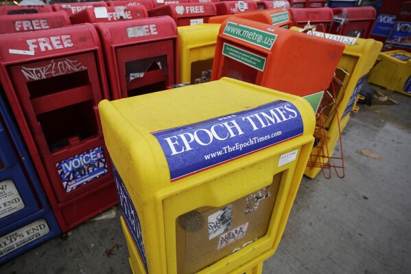 FILE - Plastic newspaper racks for The Epoch Times, The Village Voice and other newspapers stand along a Manhattan sidewalk, Wednesday, Nov. 27, 2013 in New York. The arrest of an executive at The Epoch Times in a money-laundering scheme this week has drawn attention to a media outlet that has largely lived in the shadows between its founding in 2000 and a transformation during the Trump administration. (AP Photo/Mark Lennihan, File)