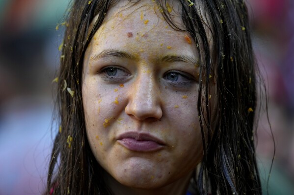 A girl reacts as her face is covered with orange juice during the "Battle of the Oranges" where people pelt each other with oranges as part of Carnival celebrations in the northern Italian Piedmont town of Ivrea, Italy, Tuesday, Feb. 13, 2024. (AP Photo/Antonio Calanni)