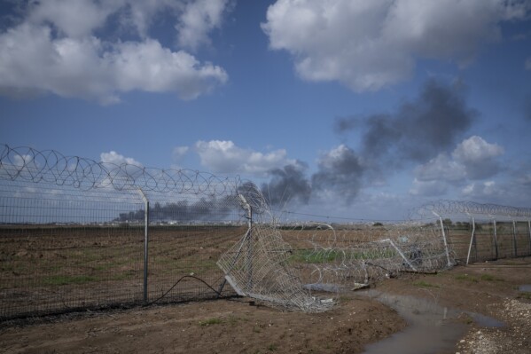 Smoke rises from the north of the Gaza Strip on Jan. 30, 2024, seen behind a gap in the fence of the Israeli Kibbutz Nahal Oz that was opened by Hamas attackers on Oct. 7, 2023, during a cross border assault. Kibbutz members installed coils of barbed wire to fill the breach. (AP Photo/Sam McNeil)