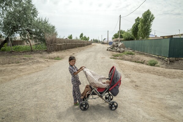 A little girl takes care of a child in Aralsk village, near Muynak, Uzbekistan, Wednesday, June 28, 2023. (AP Photo/Ebrahim Noroozi)