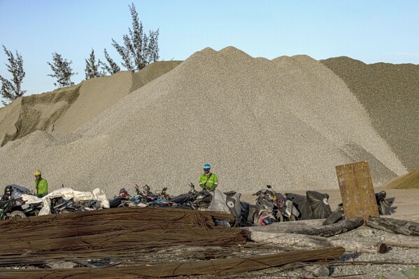 Workers stand near mounds of building materials at the construction site of the Kalimantan Industrial Park Indonesia (KIPI) in Mangkupadi, North Kalimantan, Indonesia on Thursday, Aug. 24, 2023. The industrial park being built in Indonesia on the tropical island of Borneo that has attracted billions of dollars in foreign and domestic investment is damaging the environment in an area where endangered species live and migrate. (AP Photo/Yusuf Wahil)