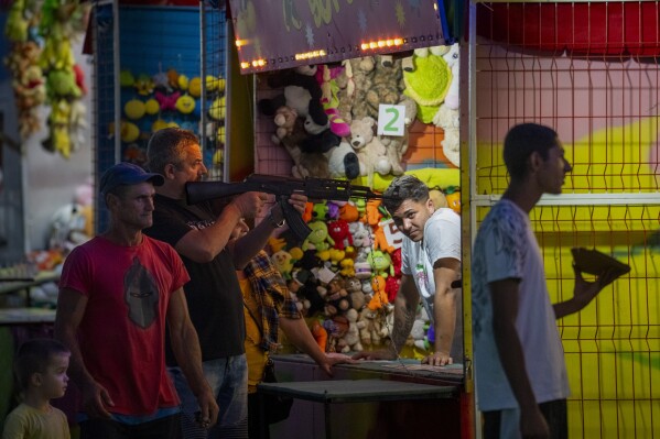 A man shoots an air soft weapon at a fair in Hagioaica, Romania, Thursday, Sept. 14, 2023. For many families in poorer areas of the country, Romania's autumn fairs, like the Titu Fair, are one of the very few still affordable entertainment events of the year. (AP Photo/Vadim Ghirda)