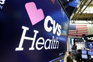 FILE - In this Dec. 4, 2017 file photo, the CVS Health logo appears above a trading post on the floor of the New York Stock Exchange.  CVS Health’s Aetna is waiving patient payments for hospital stays tied to the coronavirus. CVS Health’s Aetna said Wednesday, March 25, 2020  that many of its customers will not have to make co-payments or other forms of cost sharing if they wind up admitted to a hospital in the insurer’s provider network. (AP Photo/Richard Drew, File)