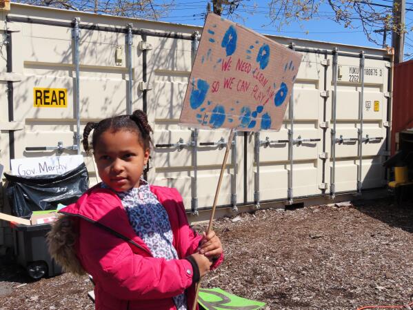 Eight-year-old Sapphire Tate holds a sign before a protest against a proposed backup power plant for a sewage treatment facility in Newark, N.J., on Wednesday, April 20, 2022. The Passaic Valley Sewerage Commission is pushing forward with the gas-fired power plant just months after New Jersey Gov. Phil Murphy ordered them to pause it to ensure that the project does not violate a soon-to-take-effect environmental justice law designed to protect communities that are already overburdened with sources of pollution. (AP Photo/Wayne Parry)