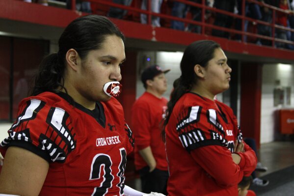In this Nov. 8, 2019 photo, Jayton Pease, left, waits to get on the field alongside his brother Jashawn, before the All Nations Football Conference championship in Vermillion, S.D.  Jashawn and Jayton Pease shed tears as the Crow Creek Chieftains won the first All Nations Conference championship, and then remembered their older brother one of too many American Indians to die by suicide on a reservation with the highest suicide rate in South Dakota. (AP Photo/Stephen Groves)