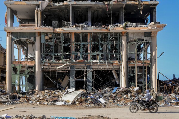 Palestinians ride a motorcycle by a destroyed building in Gaza City on Wednesday, Nov. 29, 2023, the sixth day of the temporary ceasefire between Hamas and Israel. International mediators on Wednesday worked to extend the truce in Gaza, encouraging Hamas militants to keep freeing hostages in exchange for the release of Palestinian prisoners and further relief from Israel's air and ground offensive.(AP Photo/Mohammed Hajjar)