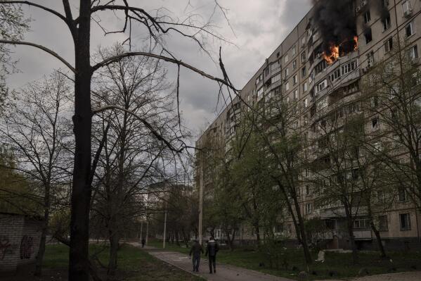 People walk near an apartment on fire after it was hit during a Russian bombardment in Kharkiv, Ukraine, Friday, April 22, 2022. (AP Photo/Felipe Dana)