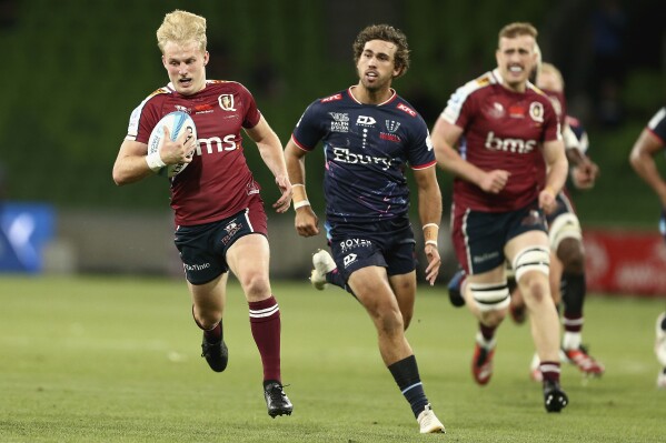 Tom Lynagh, left, of the Queensland Reds runs with the ball during the Super Rugby Pacific match between the Melbourne Rebels and the Queensland Reds in Melbourne, Australia, Friday, March 15, 2024. (Rob Prezioso/AAP Image via AP)