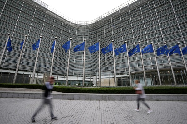 FILE - European Union flags wave in the wind as pedestrians walk by EU headquarters in Brussels, on Sept. 20, 2023. Three of the world's biggest porn websites face new requirements in the European Union including verifying the ages of users, the bloc said Wednesday, Dec. 20, 2023, as it expanded the reach of its digital law designed to keep people safe on the internet. (APPhoto/Virginia Mayo, File)