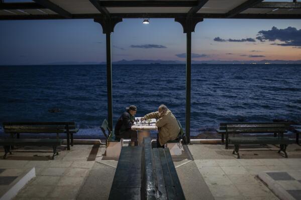 Two men wearing protective face masks play chess in Alimos, a seaside suburb of Athens, on Tuesday, April 20, 2021. (AP Photo/Petros Giannakouris)
