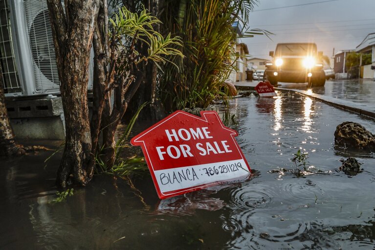 A "for sale" sign is posted in a flooded area of Holiday Acres Mobile Home Park in Hialeah, Fla. on Wednesday, June 12, 2024. The annual rainy season has arrived with a wallop in much of Florida, where a disorganized disturbance of tropical weather from the Gulf of Mexico has caused street flooding and triggered tornado watches but so far has not caused major damage or injuries. (Al Diaz/Miami Herald via AP)