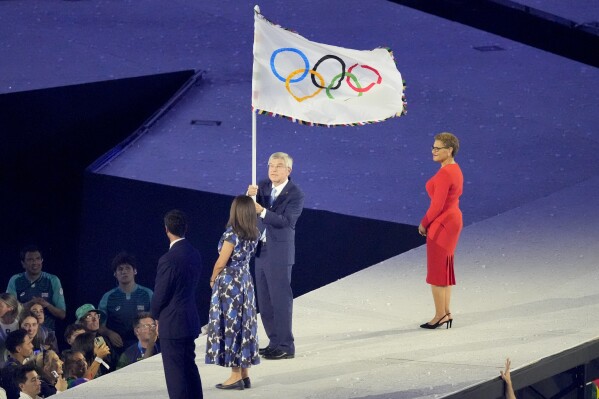 IOC President Thomas Bach holds the Olympic flag during the 2024 Summer Olympics closing ceremony at the Stade de France, Sunday, Aug. 11, 2024, in Saint-Denis, France. (AP Photo/Martin Meissner)