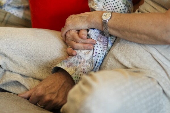 Anett Bommer holds the arm of her husband Michael Bommer, who is terminally ill with colon cancer, during a meeting with The Associated Press at his home in Berlin, Germany, Wednesday, May 22, 2024. Bommer, who has only a few more weeks to live, teamed up with friend who runs the AI-powered legacy platform Eternos to "create a comprehensive, interactive AI version of himself, allowing relatives to engage with his life experiences and insights," after he has passed away. (AP Photo/Markus Schreiber)